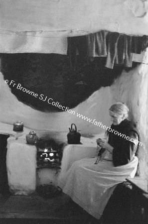 WOMAN KNITTING BY OPEN FIRE IN COTTAGE